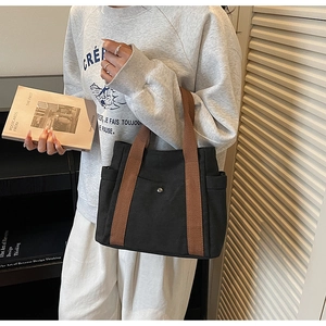 Detail of black canvas tote bag showing brown woven straps and front pocket with silver buckle