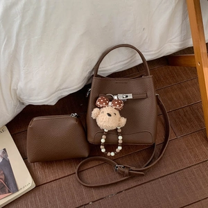 Detail of dark brown leather bucket bag with silver clasp, inner pouch, and plush bear charm