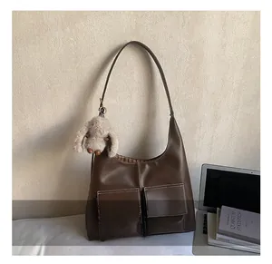 Detail view of large brown hobo bag with multi-pockets, contrast stitching, and bunny charm