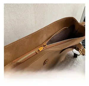 Détails d'un sac cabas en cuir marron montrant le zip doré et le pompon gris