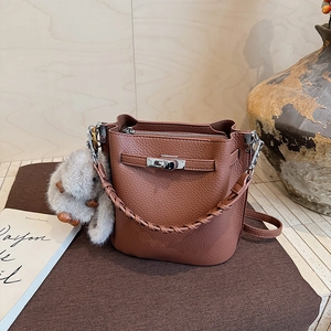 Détail d'un sac seau en cuir grainé marron avec poignée tressée et peluche décorative