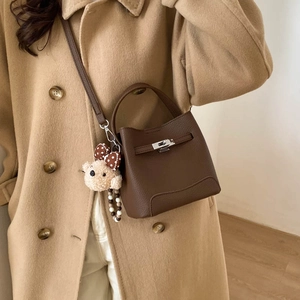 Detail of dark brown pebble leather bucket bag with metal turn-lock and teddy bear charm