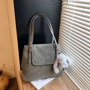 Detail of grey vintage leather tote bag with flap closure and fluffy rabbit pendant