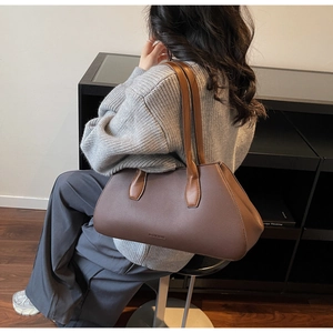 Brown textured leather tote bag with contrast straps shown on a model in a casual setting