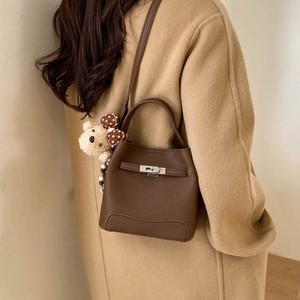 Detail of dark brown leather bucket bag with silver lock and bear charm on camel coat