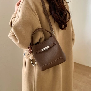 Detail of dark brown pebble leather bucket bag with metal clasp and plush bear charm
