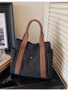 Minimalist black canvas tote bag with brown woven straps and front pocket for work