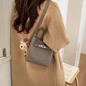 Detail of taupe pebbled leather bucket bag with metal twist lock and cute bear charm