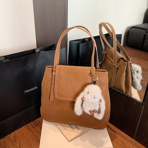 Detail of brown faux leather bucket bag with plush rabbit charm and shoulder straps