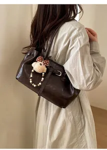 Detail of dark brown vintage faux leather shoulder bag with plush bear charm and buckle