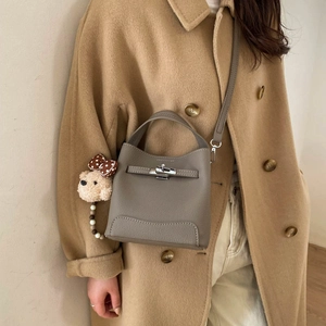 Close-up of gray pebble leather bucket bag with metallic buckle on camel coat