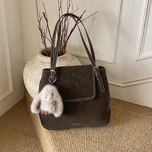 Detail of dark brown retro bucket bag with white stitching and plush bunny charm