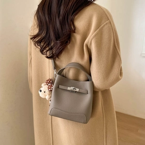 Detail view of taupe lychee leather bucket bag with metal buckle and plush bear charm