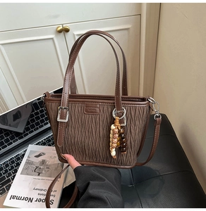 Detail view of coffee-colored pleated bucket bag with beaded charm and silver buckle