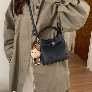 Detail of black pebbled leather bucket bag with top handle and teddy bear charm