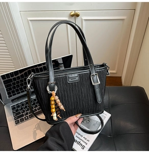 Close-up of black pleated bucket bag with wooden bead charm on a leather chair