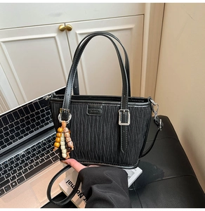 Close-up of black pleated tote bag with bead charm and detachable shoulder strap detail