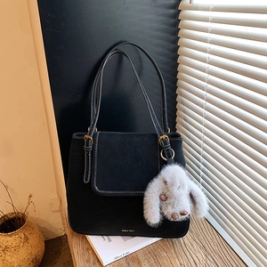 Detail of black tote bag featuring white contrast stitching and a plush bunny charm