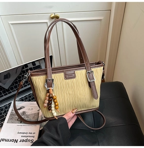 Detail of pleated fabric bucket bag with brown leather trim and wooden bead charm
