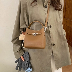 Macro detail of brown leather bucket bag featuring silver twist lock and plush bear charm
