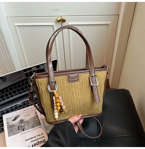 Olive green bucket bag with brown leather accents and colorful beaded charms detail