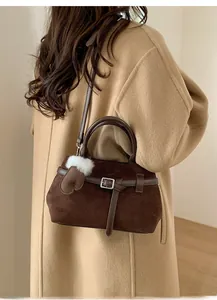 Détail d'un sac à main en daim marron avec boucle décorative et breloque peluche sur manteau