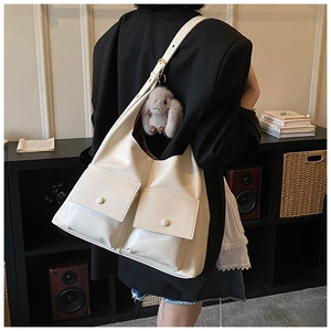 Close-up of white leather tote bag with front pockets and plush rabbit keychain accessory