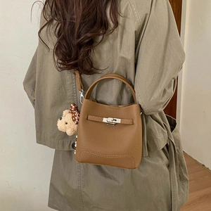 Detail of brown leather bucket bag with metal turn-lock and cute plush bear charm