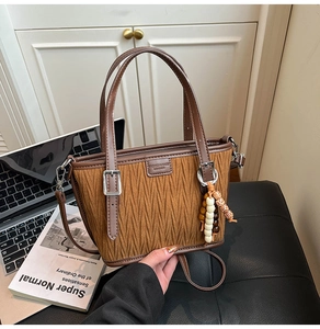 Close-up of brown pleated bucket bag with beaded tassel and adjustable shoulder strap