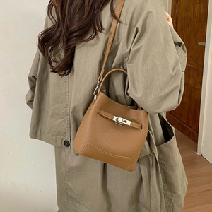 Brown litchi leather bucket bag with silver lock shown on a model in a minimalist room