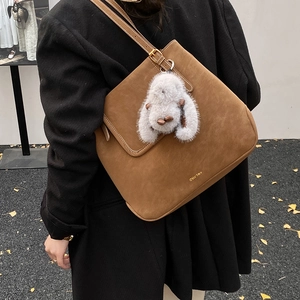 Detail of a brown suede bucket bag with a plush rabbit charm and adjustable shoulder strap