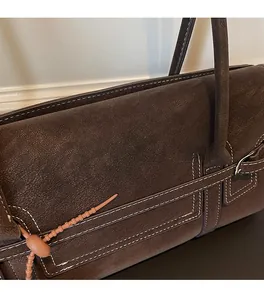 Close-up of textured dark brown leather tote with white contrast stitching and charm