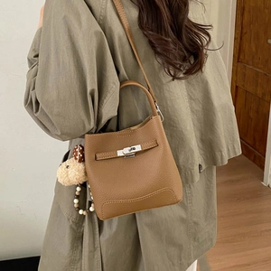 Brown lychee leather bucket bag detail with plush dog charm and silver buckle