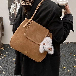 Brown leather tote bag with plush rabbit charm shown on model in outdoor setting