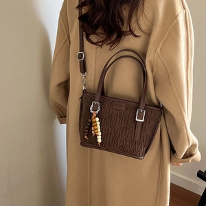 Detail of dark brown pleated leather bucket bag with bead charm and shoulder strap