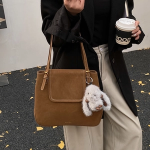 Brown suede bucket bag with plush bunny charm shown against an autumn ginkgo leaves background