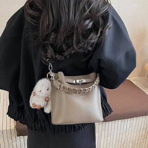 Détail d'un sac seau en cuir grainé gris-brun avec anse tressée et breloque lapin