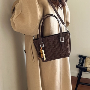 Detail of coffee matelassé bucket bag featuring pleated leather and wooden bead charm
