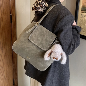 Detail of dark green suede tote bag featuring gold logo and cute rabbit plush charm
