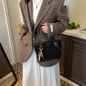 Close-up of a black pleated bucket bag with ethnic wooden bead charm on a brown blazer