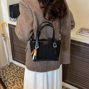 Detail view of black pleated bucket bag with vintage bead charm and silver hardware
