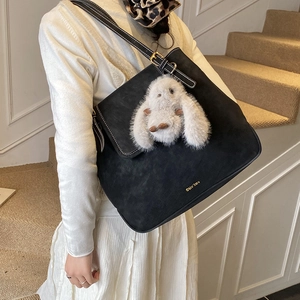 Detail of black suede bucket bag with contrast stitching and plush bunny charm