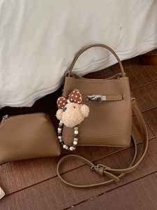 Brown litchi grain bucket bag set with silver hardware and bear charm on wooden floor