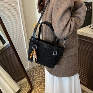 Detail of black pleated bucket bag featuring ethnic bead charm and soft texture finish
