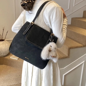 Detail of black suede tote bag with contrast stitching and rabbit plush charm on a shoulder strap