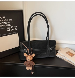 Close-up of black tote bag with white contrast stitching and a plush bear charm detail