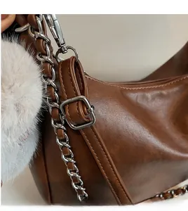 Detail of adjustable leather shoulder strap and silver chain on brown baguette bag
