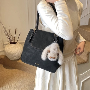Close-up of black suede tote bag with golden logo, white stitching, and plush rabbit charm