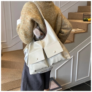 Detail of a creamy white large tote bag with dual front pockets and soft matte leather texture
