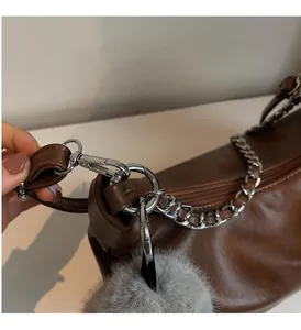 Detail of glossy brown leather bag with silver chain strap and grey plush charm